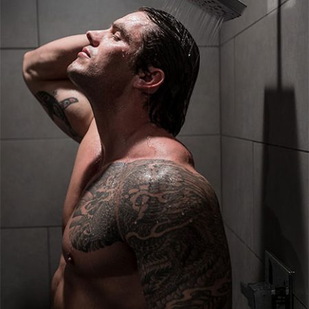 Man with tattooed arm relaxing under a shower after a recovery treatment