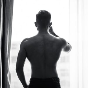 Shirtless man standing near a window