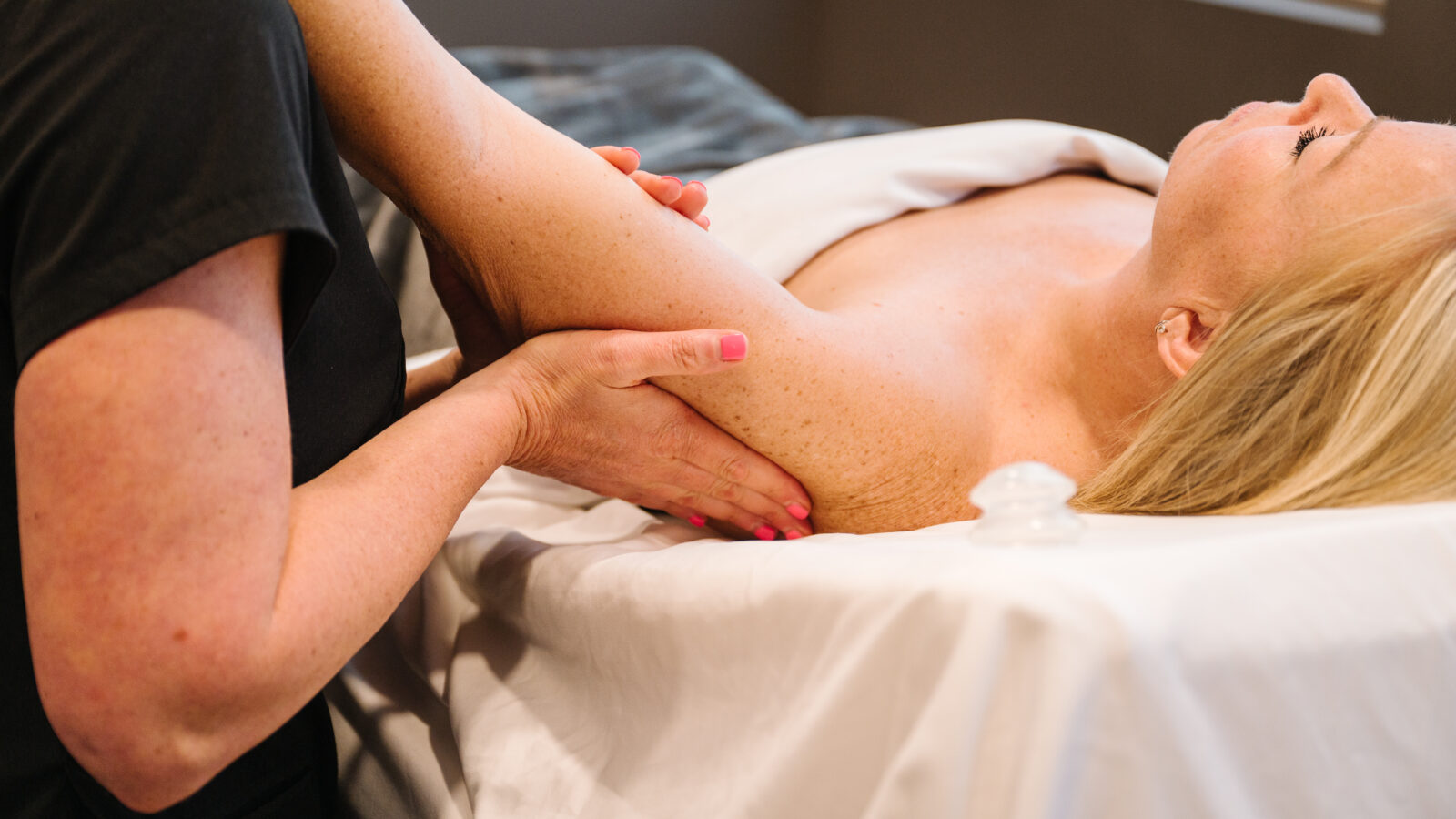 A woman receives a relaxing massage on her arm while lying on a massage table